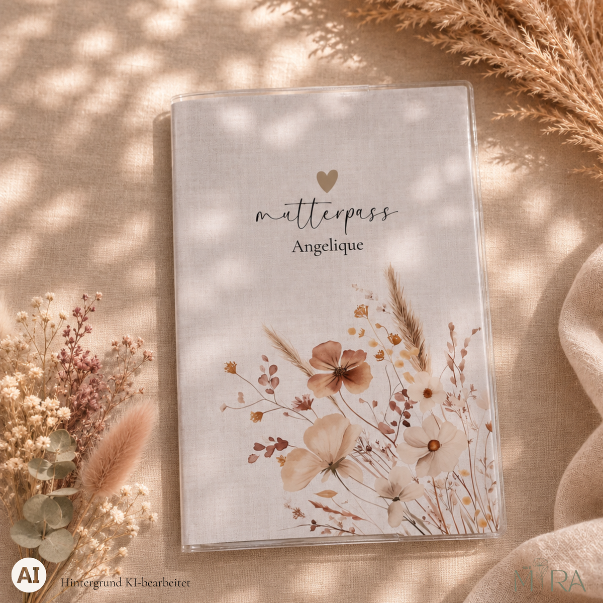 Personalisierte Mutterpasshülle „Elin“ mit getrockneten Blumen im Vintage-Look, seitlich aufsteigend, und Schriftzug „mutterpass Angelique“ auf hellem Untergrund – ma e mira